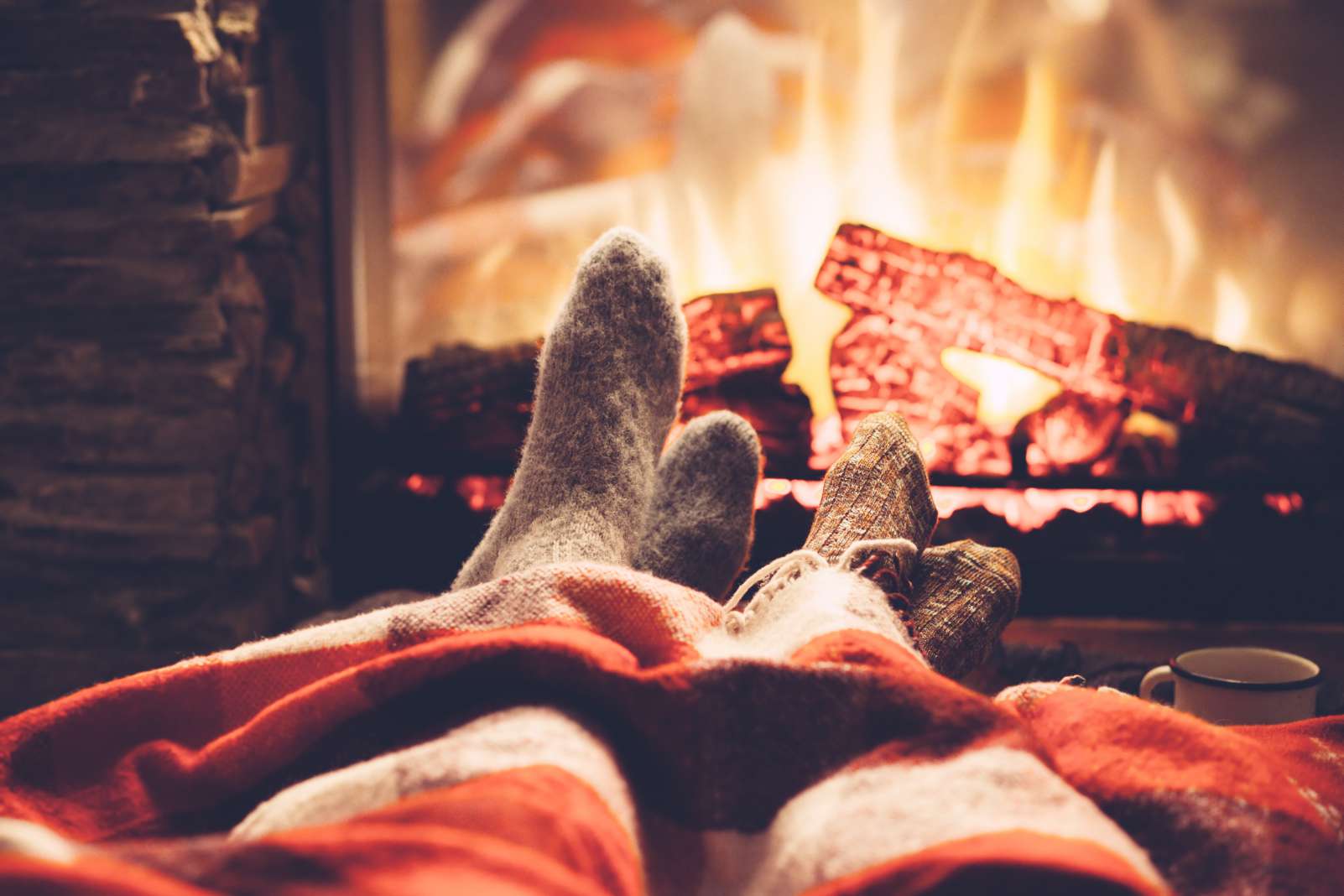 Cold fall or winter evening in Canada. People resting by the fire with blanket and tea. Closeup photo of feet in woolen socks. Cozy scene.